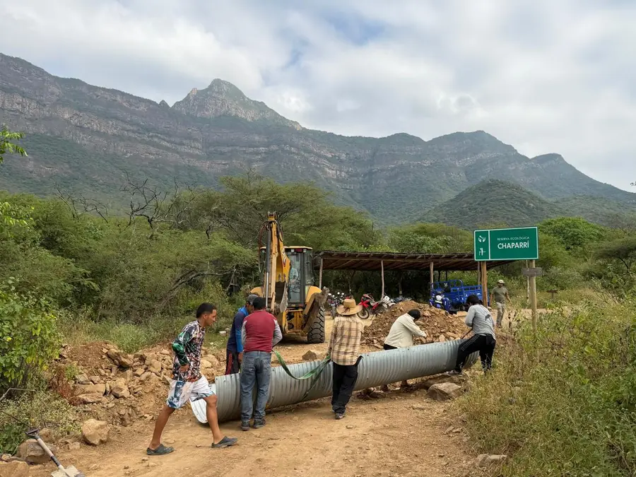 Operai e comuneros posizionano un grande tubo metallico accanto al cartello della Riserva Ecologica Chaparri, ai piedi della montagna