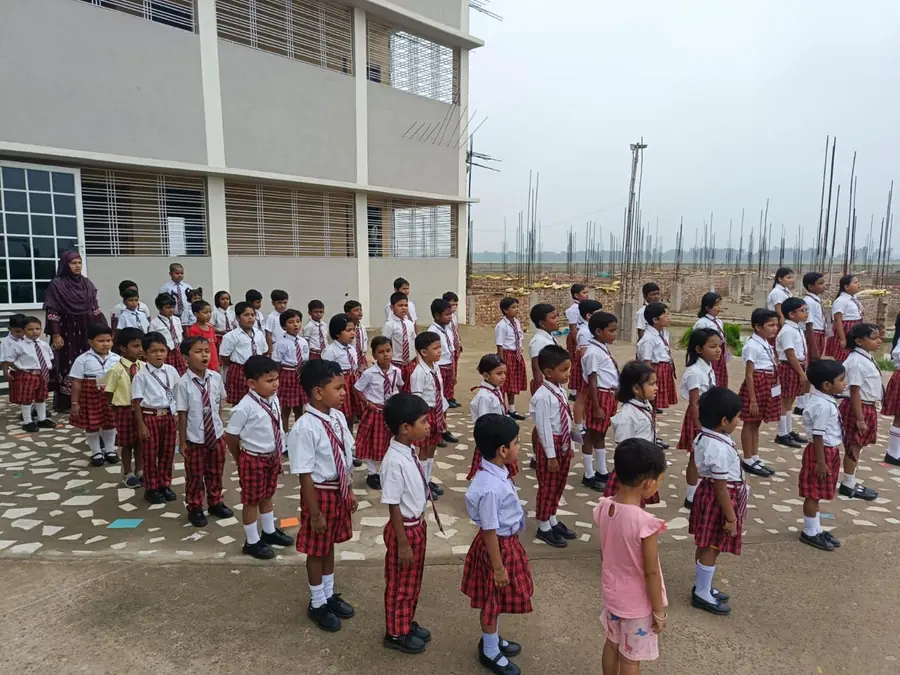 L'assemblea del mattino alla SREE International School: una sessantina di bambini in divisa davanti all'edificio finito, e sulla destra i ferri d'armatura della nuova ala che aspetta di essere costruita