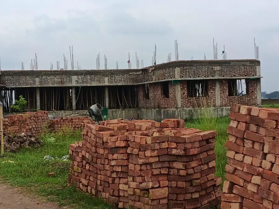 Struttura grezza in mattoni delle nuove aule della SREE International School, con i ferri dei pilastri che sporgono e le cataste di mattoni in primo piano