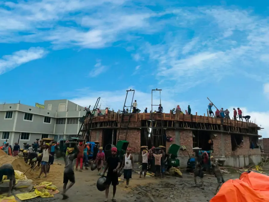 Decine di operai al lavoro sulla nuova ala in mattoni della scuola, accanto all’edificio bianco già funzionante